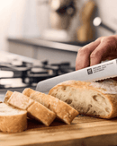 Couteau à pain Four Star Zwilling sur planche entrain de couper le pain