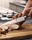 Couteau à trancher ZWILLING Four Star en action, découpant de la viande sur une planche en bois.