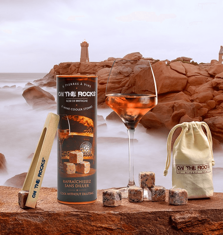 Coffret pierres à vin en granit rose de Bretagne avec pince, à côté d'un verre de rosé en bord de mer.