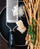 Râpe à gros grains MICROPLANE avec fromage et bâtonnets de pain, idéale pour râper des ingrédients.