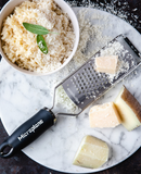 Râpe étoiles MICROPLANE sur une planche avec fromage et risotto, idéale pour râper fromage et agrumes.