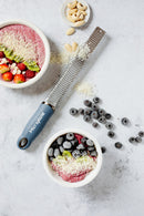 Zesteur Microplane on a countertop next to bowls of smoothie topped with fruits and nuts.