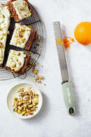 Zesteur Premium Classic Microplane grating orange zest next to dessert topped with pistachios.
