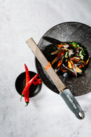 Zesteur Premium Classic Microplane next to a plate of mussels and red chilies, showcasing precision and culinary elegance.