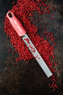 Zesteur Premium Classic Microplane with pink handle surrounded by red pepper berries on a dark background.