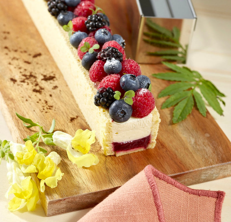 Gouttière à bûche avec fruits rouges sur un plateau en bois, décorée avec des fleurs.