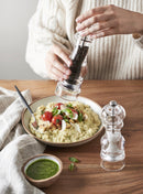 Person using a Moulin à Sel to season a plate of risotto with vegetables and herbs.